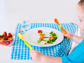 Bebé comiendo alimentos para bebés de 24 meses con cubiertos en un mantel azul 