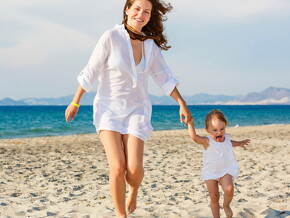 Mamá con bebe caminando y jugando en la playa cuidan de su salud