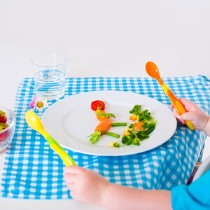 Bebé comiendo alimentos para bebés de 24 meses con cubiertos en un mantel azul 