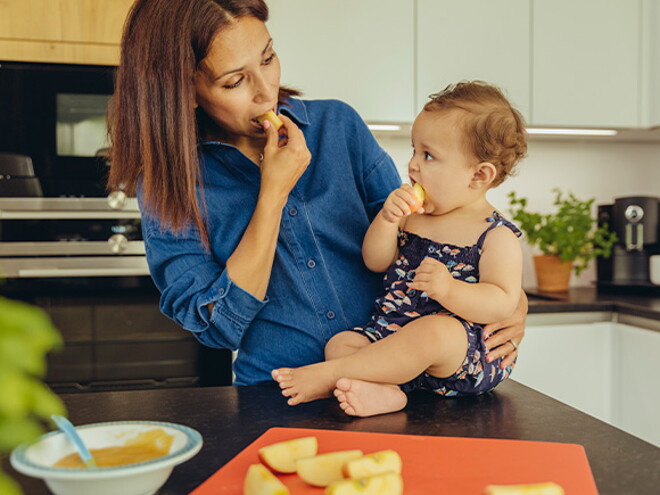 Mamá y bebé comiendo fruta en la cocina.